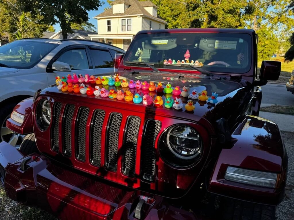 A collection of colorful rubber ducks arranged on the hood of a red Jeep, creating a playful "ducking" display.