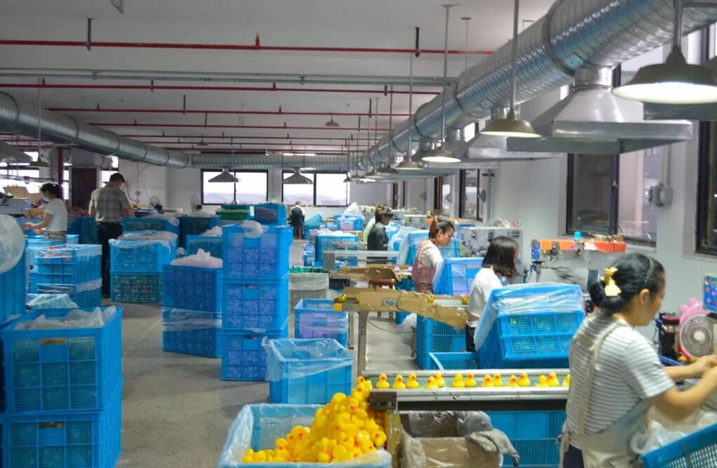 Rubber duck production line in a factory, with workers assembling and packaging rubber ducks in blue baskets.