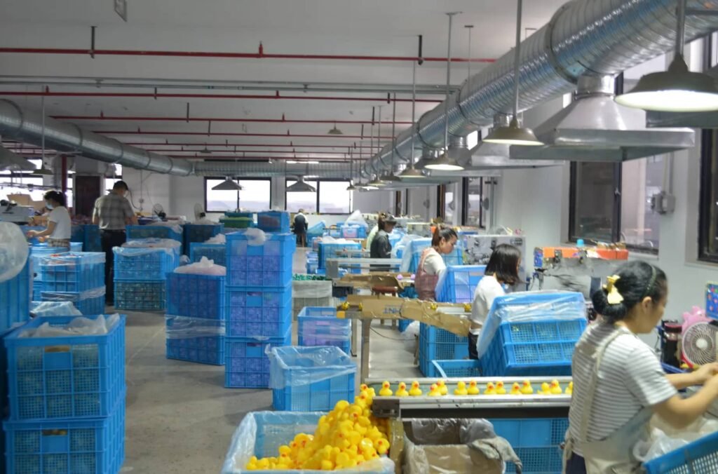 Rubber duck manufacturing line with workers assembling and packaging products, surrounded by storage bins.