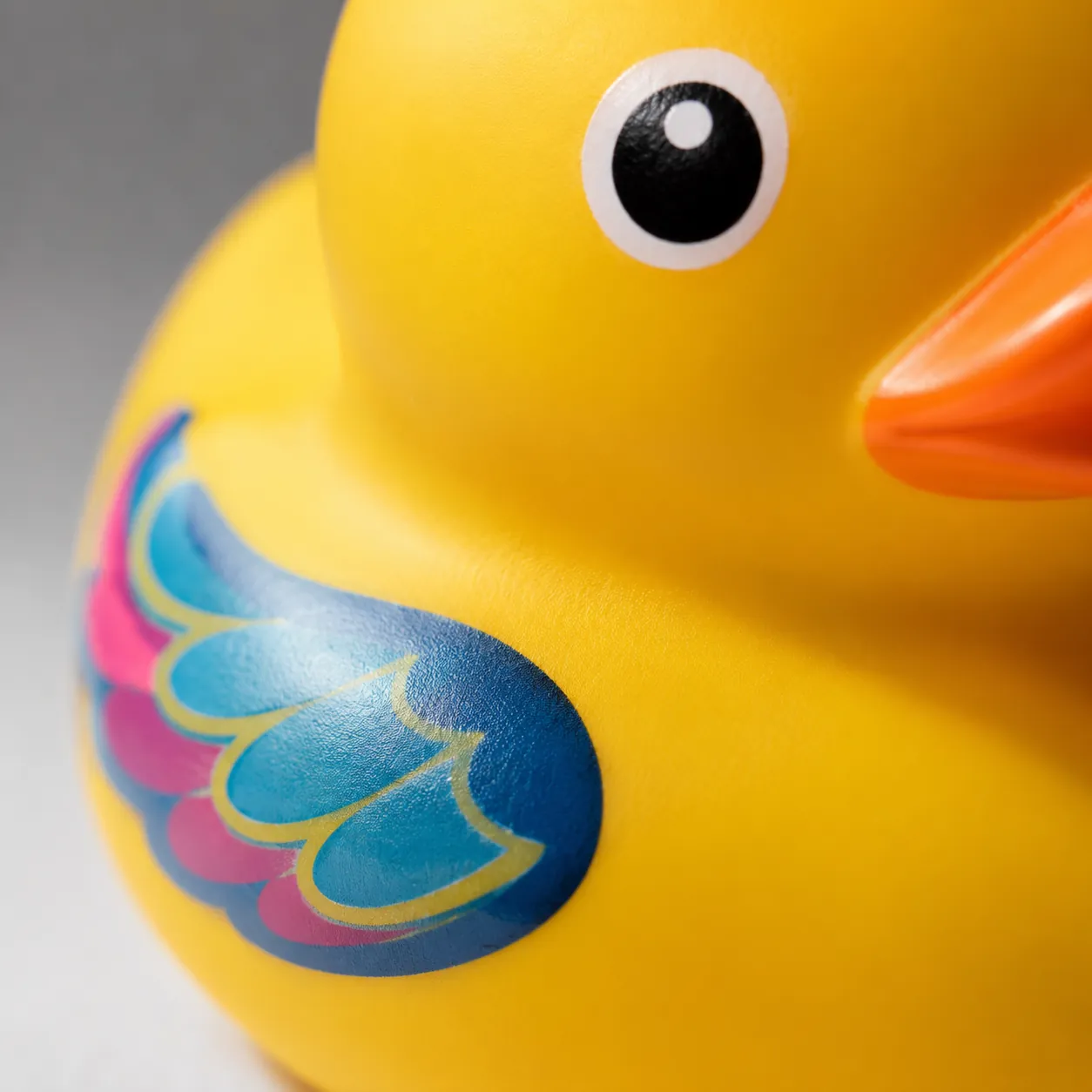 Hyper-realistic product photography, extreme close-up of a rubber duck's side showing fine full-color printing details and smooth phthalate-free PVC texture, soft ring light reflection, macro lens, shallow depth of field, no text, no brand logo