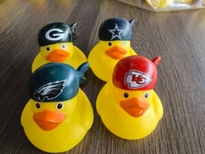 Four custom yellow rubber ducks wearing colored caps with printed logo artwork